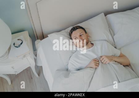 Vista dall'alto di stressato giovane maschio caucasico sdraiato a letto con gli occhi aperti e incapace di dormire, l'uomo che si sente infelice e stanco da insomni Foto Stock