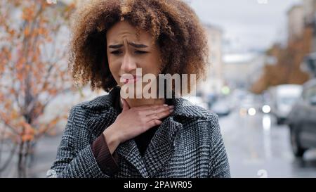 Ritratto afro americano che soffre di tonsillite angina in piedi all'aperto ritratto donna malsana toccare collo sente disagio sentimenti dolorosi Foto Stock