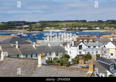 Isole di Scilly, Regno Unito - vista sui tetti di Hugh Town con barche a vela ancorati nel porto sullo sfondo Foto Stock