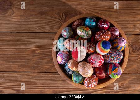 Una ciotola di legno con uova di Pasqua ben disposte si trova su uno sfondo di tavole. Foto Stock