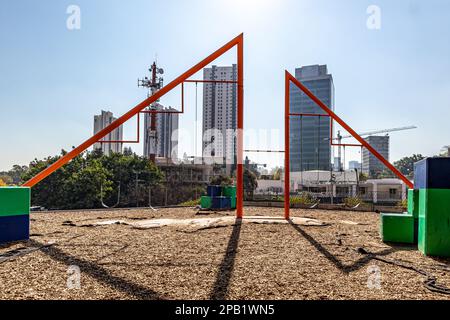 Parco giochi con altalene vuote nel centro commerciale con edifici in sfondo sfocato contro un cielo blu, area pubblica per famiglie per il divertimento, soleggiato d Foto Stock