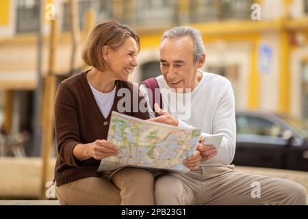 Happy Senior Couple Holding Mappa dei viaggi seduti all'aperto Foto Stock