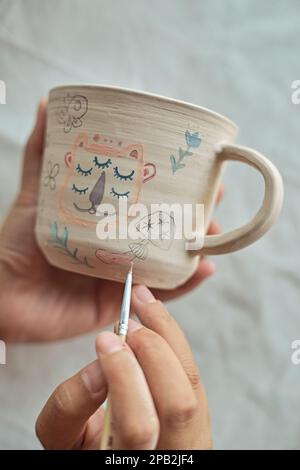 Primo piano di una donna vasaio pittura una tazza nel suo laboratorio di artigianato. Foto Stock