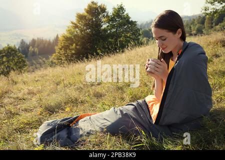 Giovane donna con drink in sacco a pelo circondato da una bella natura Foto Stock