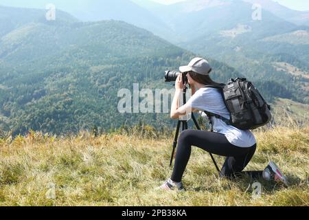 Donna che scatta foto del paesaggio montano con una fotocamera moderna su un cavalletto all'aperto Foto Stock