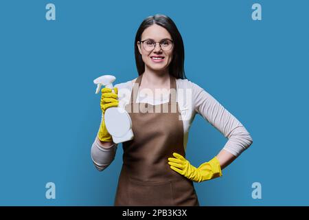 Giovane donna in grembiule guanti con detergente organico su sfondo blu Foto Stock