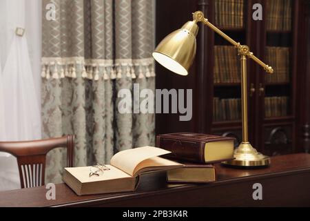 Libri, bicchieri e lampada su tavolo in legno nella sala lettura biblioteca Foto Stock