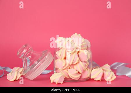 Vaso in vetro con gustose marshmallow su sfondo rosa brillante Foto Stock