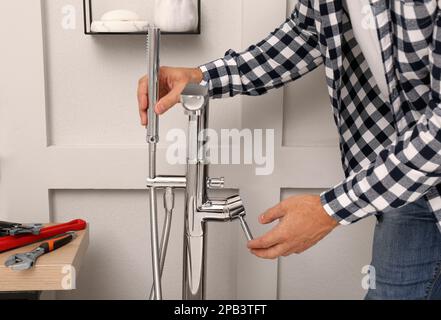 Uomo che installa il rubinetto dell'acqua con soffione doccia in bagno, closeup Foto Stock