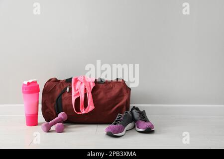 Borsa rossa e accessori sportivi sul pavimento vicino alla parete della luce, spazio per il testo Foto Stock