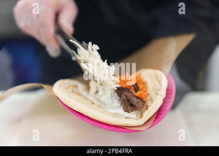 Il cuoco mette il cavolo sul pane pita con carne di pollo alla griglia. Lo chef prepara gyros greci tradizionali per il pranzo Foto Stock