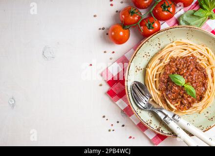 Pasta italiana bolognese. Spaghetti con sugo di carne e pomodoro in un piatto con tovaglia italiana su fondo bianco di legno. Con tomat di ciliegia fresca Foto Stock