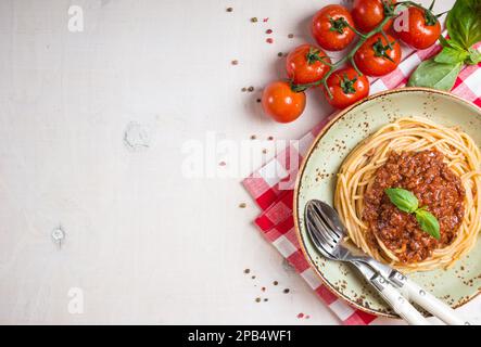 Pasta italiana bolognese. Spaghetti con sugo di carne e pomodoro in un piatto con tovaglia italiana su fondo bianco di legno. Con tomat di ciliegia fresca Foto Stock