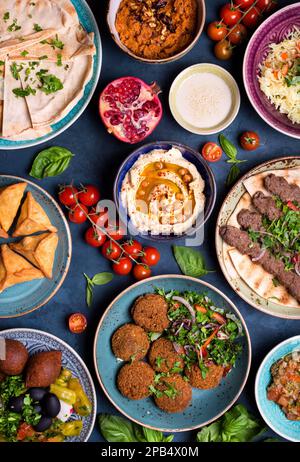 Medio orientale o piatti arabi e un assortimento di meze, concreto sfondo rustico. Spiedini di carne, falafel, Baba ghanoush, muhammara, hummus, sambusak, riso, Foto Stock