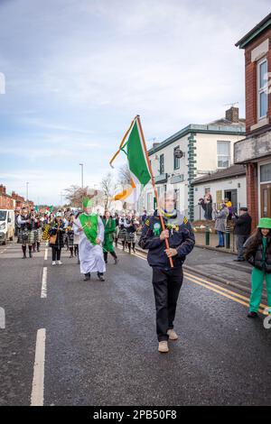 Warrington, Cheshire, Regno Unito - 12 marzo 2023 – il Warrington Irish Club ospita il St. La parata del giorno di Patrick. A partire dalle 10,30 del mattino dall'Irish Club di Orford Lane fino al "River of Life" di Bridge Street, nel centro della città, dove si è svolto un breve servizio per ricordare l'anniversario del bombardamento di Warrington. La bandiera irlandese guidò la sfilata seguita da un uomo vestito come San Patrizio Foto Stock