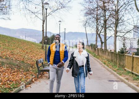Una coppia multiculturale e vivace che si attraversa un colorato parco autunnale Foto Stock