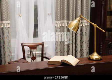 Libro e lampada su tavolo in legno nella sala lettura biblioteca Foto Stock