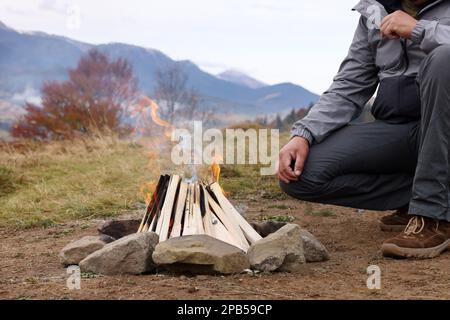 Uomo vicino falò in montagna, primo piano. Stagione Campeggio Foto Stock