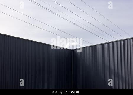 Angolo di un edificio industriale in ferro ondulato e linee elettriche contro il cielo Foto Stock