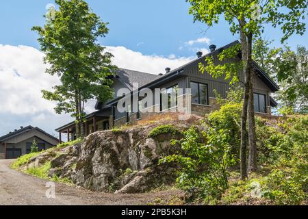 Taglio pietra e carboncino in legno con finitura nera struttura in legno ibrido casa costruita in cima a affioramento in estate. Foto Stock