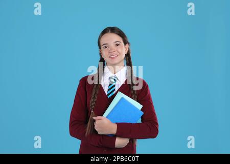 Ragazza adolescente in uniforme scolastica con libri su sfondo azzurro Foto Stock