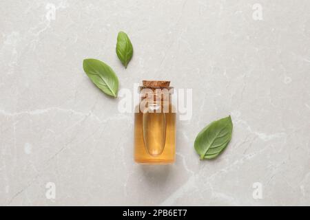 Bottiglia di olio essenziale di basilico e foglie fresche su tavola di marmo chiaro, piatto Foto Stock