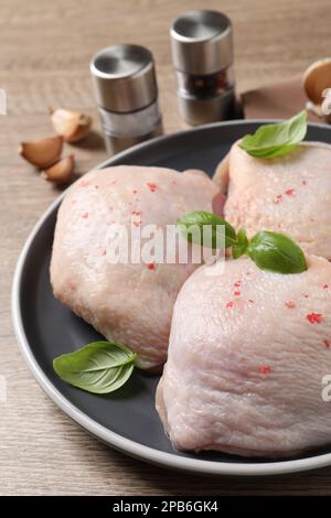 Cosce di pollo crude con basilico su tavolo di legno, primo piano Foto Stock