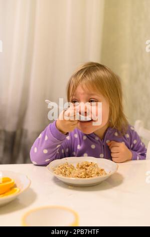 una bambina mangia porridge con un appetito Foto Stock