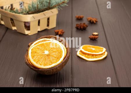 Fette secche di arancia in conchiglia di cocco. Ramo di abete in un cesto. Vista dall'alto. Sfondo di legno scuro. Foto Stock