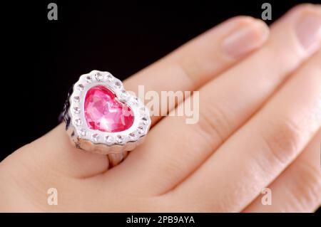 Primo piano della mano della donna con grande anello di cuore rosa, concetti di amore, doni, gioielli, argento, relazioni, incontri, impegno, moda e altro ancora Foto Stock