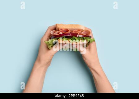 Le mani femminili tengono un delizioso sandwich al prosciutto su sfondo blu Foto Stock