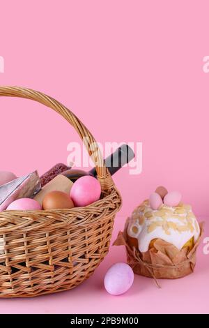 Cestino con uova di Pasqua, bottiglia di vino e torta su sfondo rosa Foto Stock