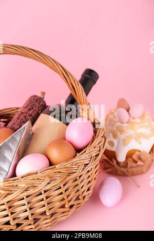 Cestino con uova di Pasqua, bottiglia di vino e torta su sfondo rosa Foto Stock