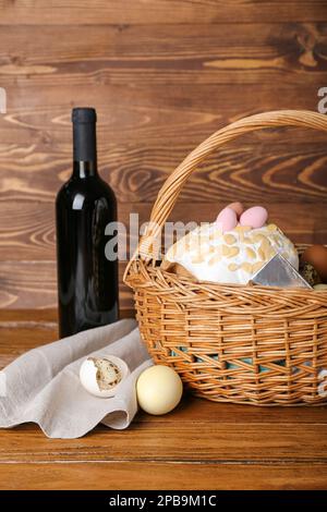 Cestino con uova di Pasqua, torta e bottiglia di vino su sfondo di legno Foto Stock