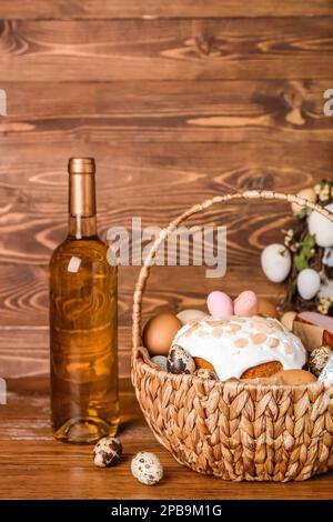 Cestino con uovo di Pasqua, torta e bottiglia di vino su sfondo di legno Foto Stock