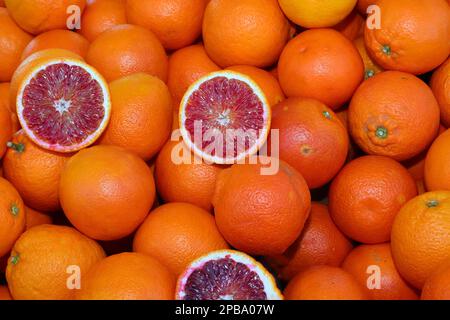 sfondo di molte arance arance mature e due metà si aprono per vedere i contenuti succosi in vendita al fruttivendolo Foto Stock