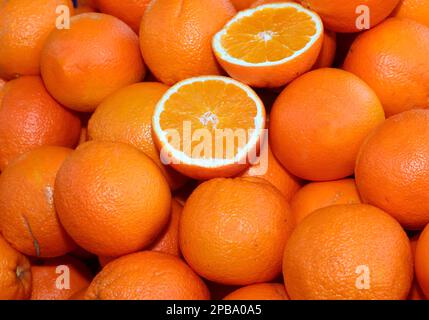 sfondo di molte arance arance mature e alcuni tagliati a metà per la vendita nel fruttivendolo Foto Stock