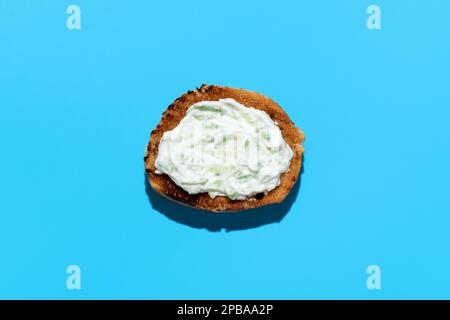 Vista dall'alto con una fetta di pane tostato con salsa tzatziki, minimalista su un tavolo blu. Delizioso spuntino, salsa tzatziki con pane, isolato o Foto Stock