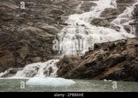 Acqua che scende lungo una scogliera rocciosa con un grower blu, vicino al ghiacciaio Jorge Montt, Patagonia Foto Stock