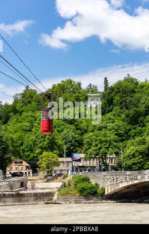 Funivia rossa Kutaisi sul fiume Rioni, lussureggianti alberi verdi, case residenziali e stazione superiore sullo sfondo. Foto Stock