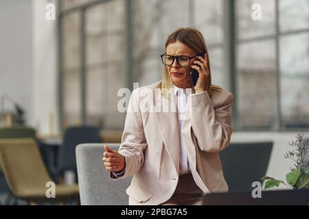 Professionista concentrato che parla al telefono con il cliente mentre si siede in un ufficio moderno Foto Stock