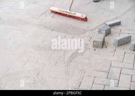 sabbia spazzante con una scopa durante la costruzione di un nuovo marciapiede Foto Stock