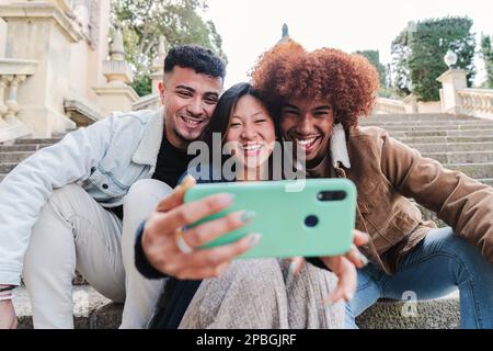 Gruppo di amici multirazziali adolescenti che si divertono a fare un ritratto selfie con un telefono cellulare. Tre giovani felici sorridono e guardano video divertenti o videochiamano con un cellulare . Foto di alta qualità Foto Stock