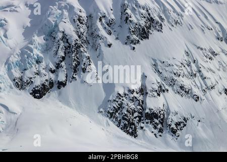 Ripido pendio sul lato di alta montagna sulla penisola antartica. Silken strato di neve, con rocce sottostanti esposte. Ghiaccio blu anche visibile. Foto Stock