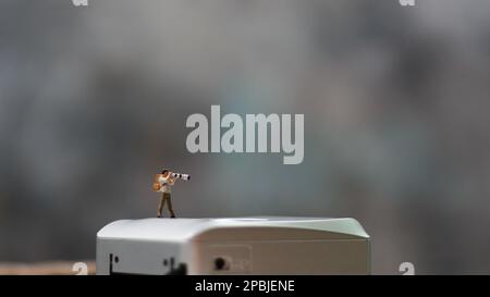 una figura in miniatura che fotografa con una fotocamera contro una fotocamera reale sullo sfondo. Foto Stock