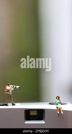 una figura in miniatura che fotografa con una fotocamera contro una fotocamera reale sullo sfondo. Foto Stock