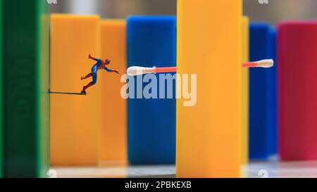 una figura umana in miniatura con il potere di un ragno che salta su un giocattolo colorato a blocchi. il loro concetto di reinventare i supereroi. Foto Stock