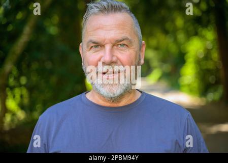 Uomo anziano intenso che guarda nella telecamera con un'espressione in attesa all'aperto in un parco Foto Stock