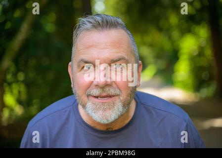 Uomo anziano intenso che guarda nella telecamera con un'espressione in attesa all'aperto in un parco Foto Stock