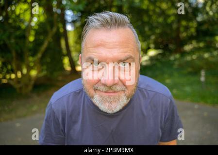 Sorridente uomo di mezza età che si inclina verso la fotocamera in un ritratto facciale corto all'aperto Foto Stock